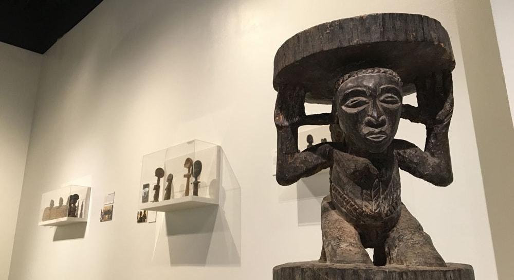 Photo of an African sculpture of a person carrying a plate on their head, in a gallery