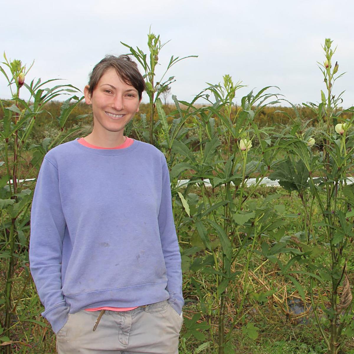 Photo of a woman standing in front of crops at Eden Hall Farm smiling.